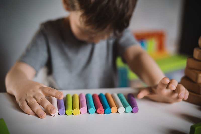 A boy with autism looks down while playing with clay during a therapy session.