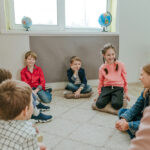 Children sit in a circle and participate in group therapy under the supervision of a therapist.