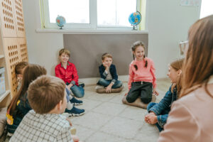 Children sit in a circle and participate in group therapy under the supervision of a therapist.